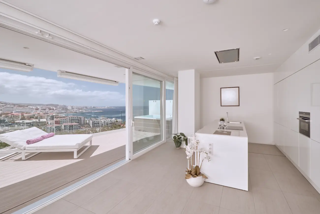 Open-plan suite with indoor seating area and direct access to a terrace overlooking the sea and surrounding landscape.