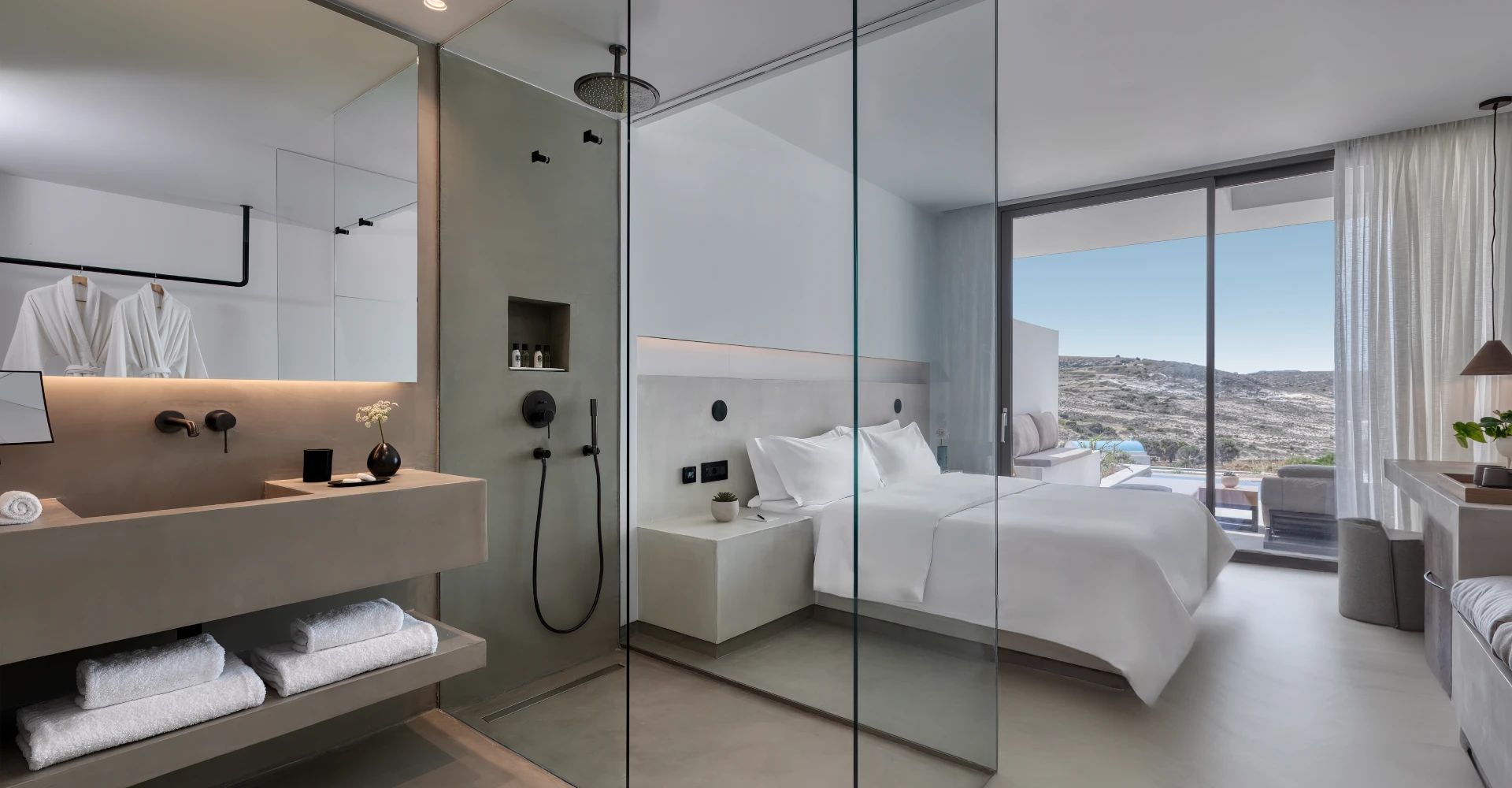 Modern open-plan suite with king bed, glass shower, and balcony view at Domes White Coast Milos.